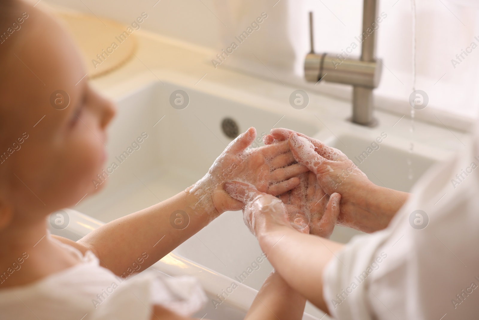 Photo of Mother and daughter washing their hands indoors, closeup