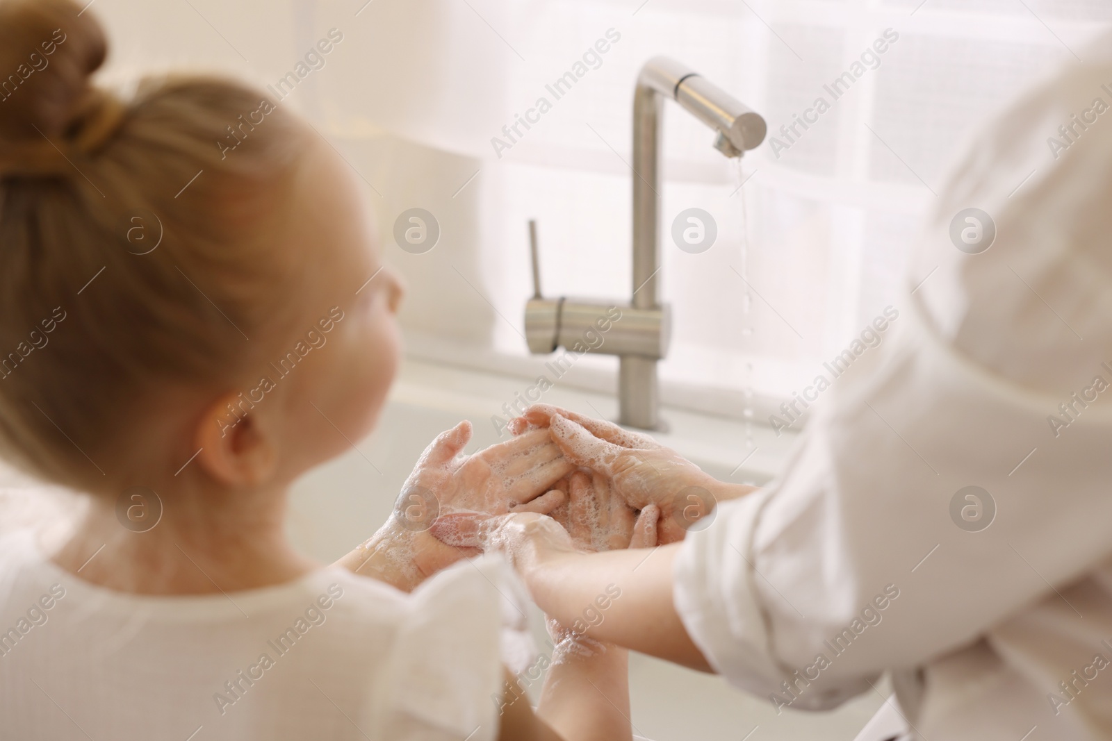 Photo of Mother and daughter washing their hands indoors, closeup