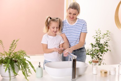 Photo of Happy mother and daughter washing their hands indoors