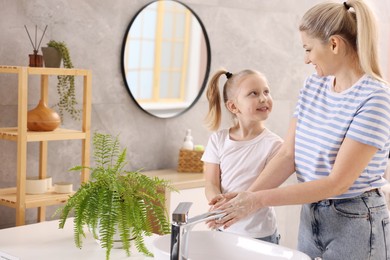 Happy mother and daughter washing their hands in bathroom