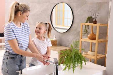 Happy mother and daughter washing their hands in bathroom