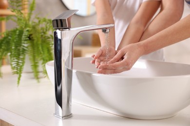 Photo of Mother and daughter washing their hands above sink indoors, closeup