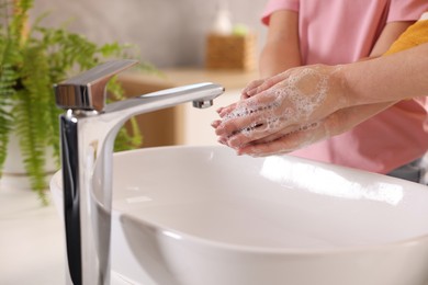 Photo of Mother and daughter washing their hands above sink indoors, closeup