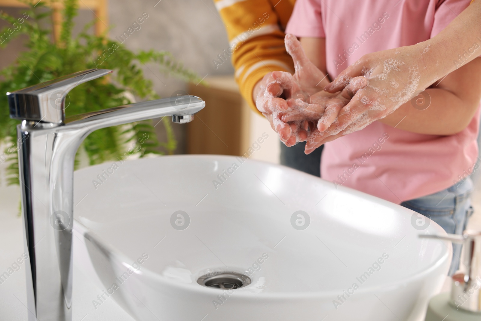 Photo of Mother and daughter washing their hands above sink indoors, closeup