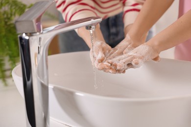 Mother and daughter washing their hands above sink indoors, closeup