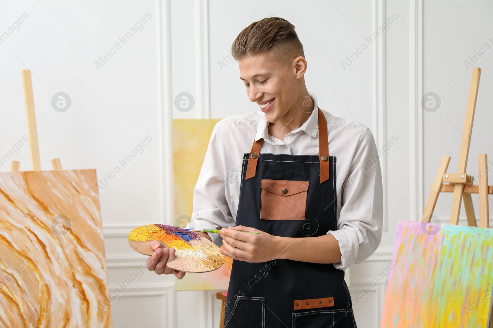 Photo of Smiling man with palette and paintbrush in workshop