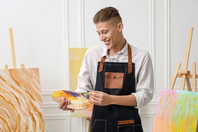 Smiling man with palette and paintbrush in workshop