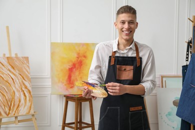 Photo of Smiling man with palette and paintbrush in workshop