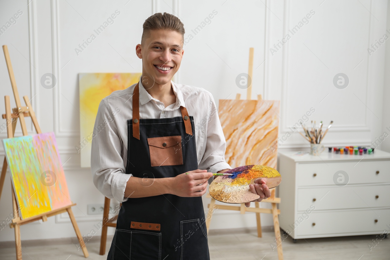 Photo of Smiling man with palette and paintbrush in workshop