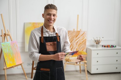 Smiling man with palette and paintbrush in workshop