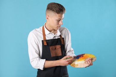 Photo of Man with palette and paintbrush on light blue background