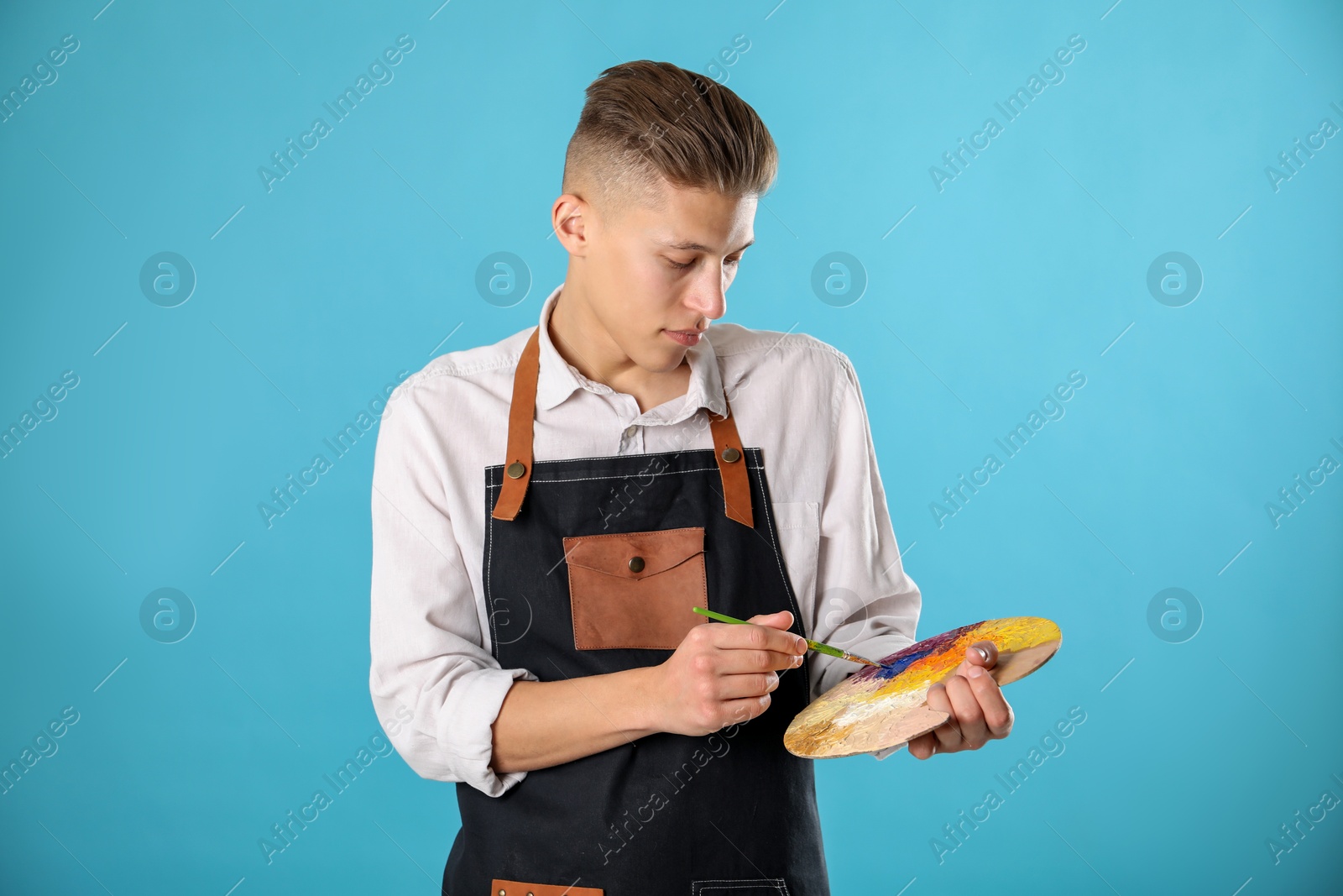 Photo of Man with palette and paintbrush on light blue background