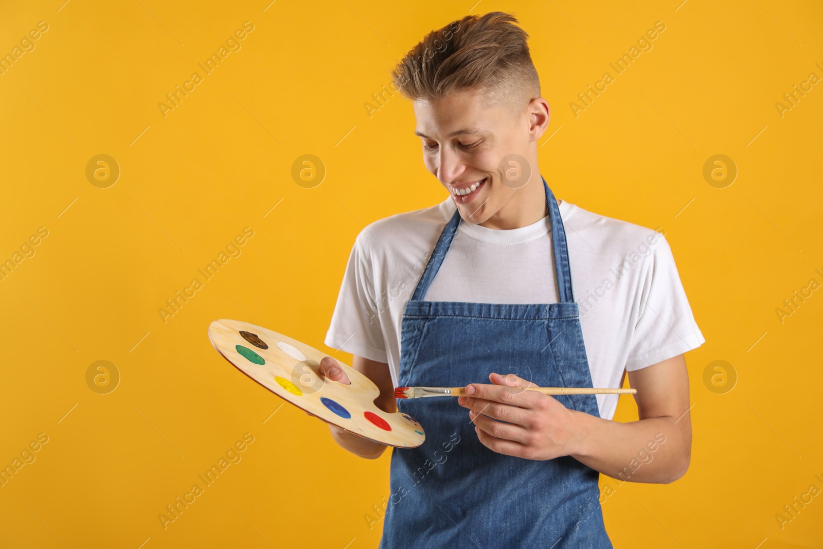 Photo of Happy man with wooden palette and paintbrush on orange background. Space for text