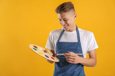 Happy man with wooden palette and paintbrush on orange background. Space for text