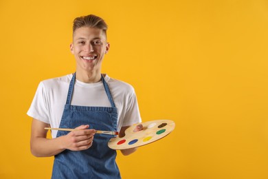 Happy man with wooden palette and paintbrush on orange background. Space for text