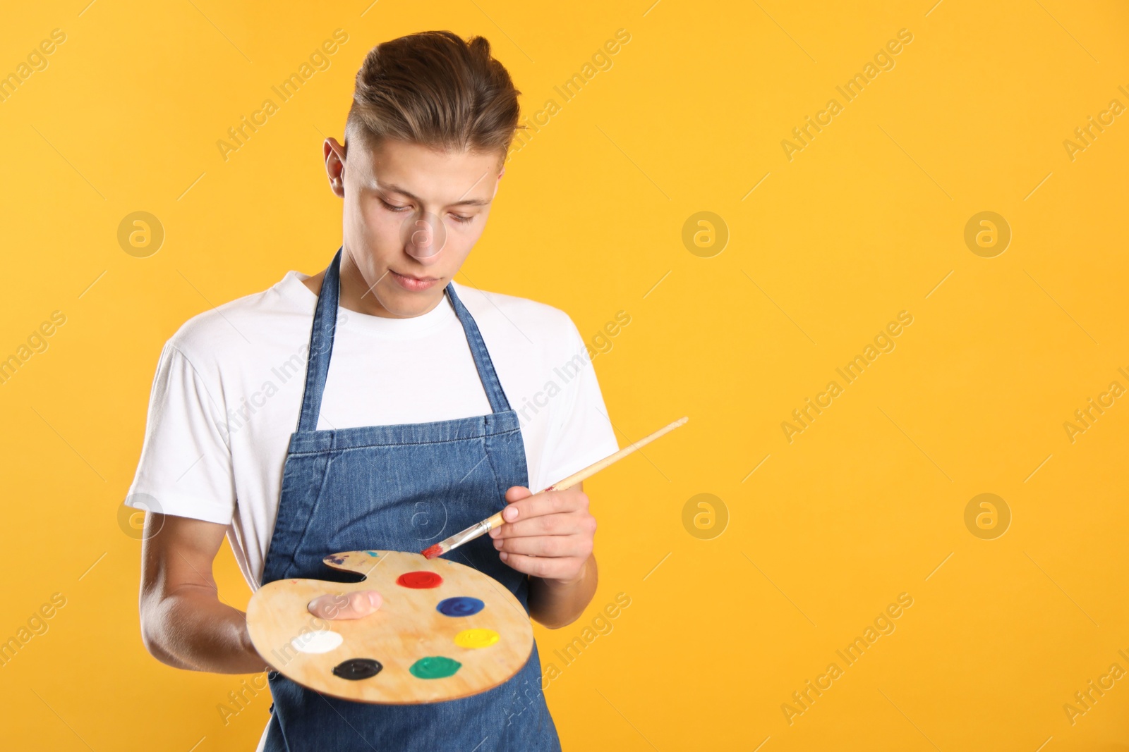 Photo of Man with wooden palette and paintbrush on orange background. Space for text