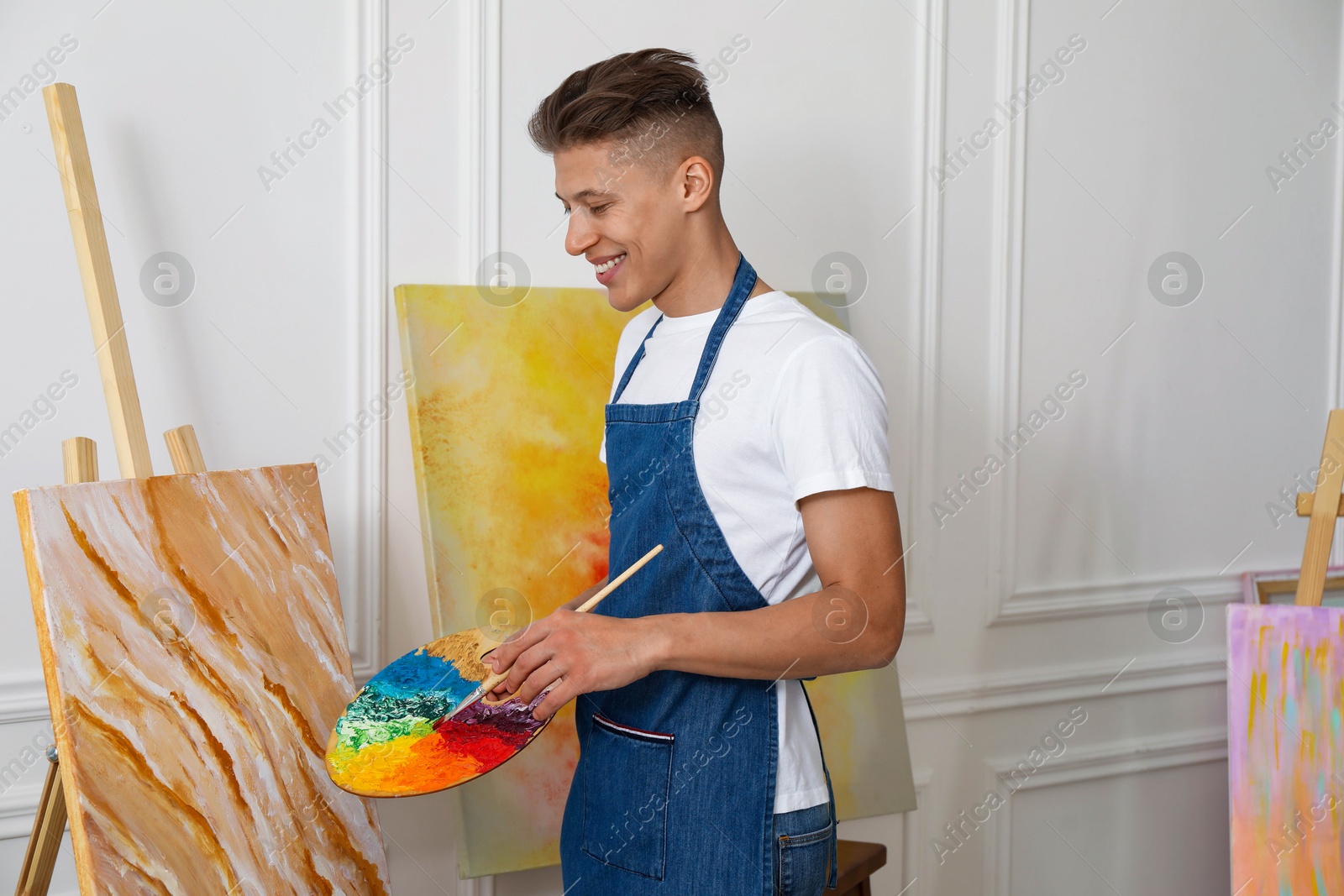 Photo of Smiling man with palette and paintbrush drawing picture indoors