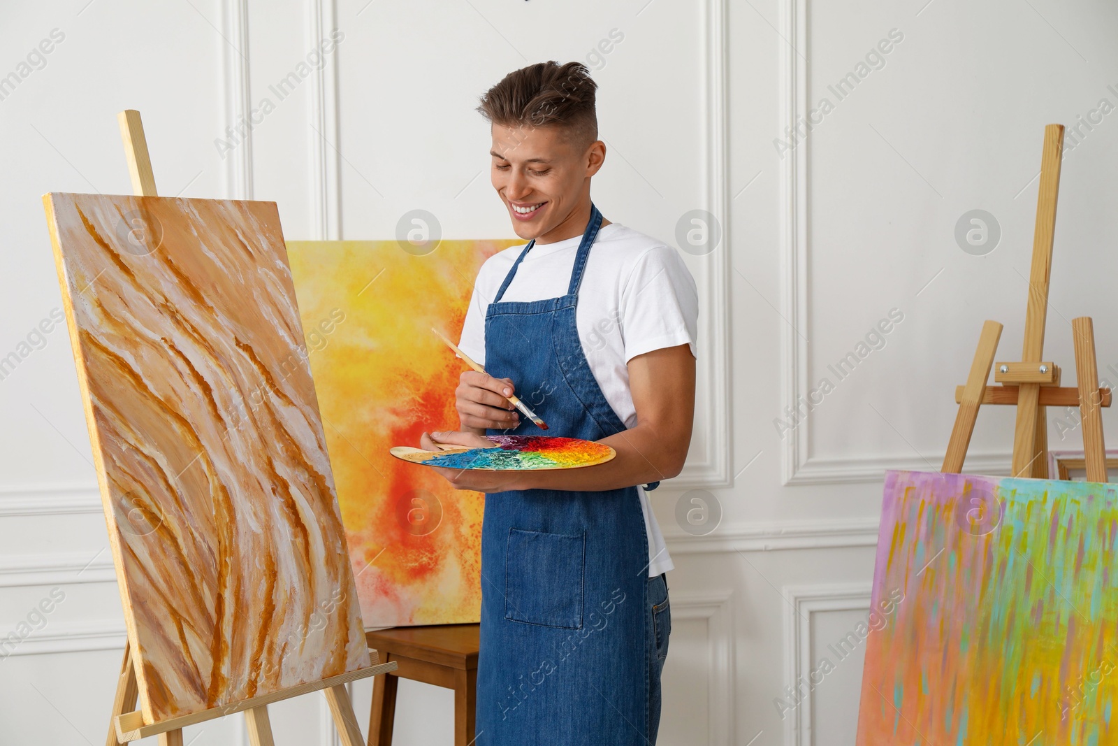 Photo of Smiling man with palette and paintbrush drawing picture indoors