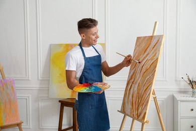 Photo of Smiling man with palette and paintbrush drawing picture indoors