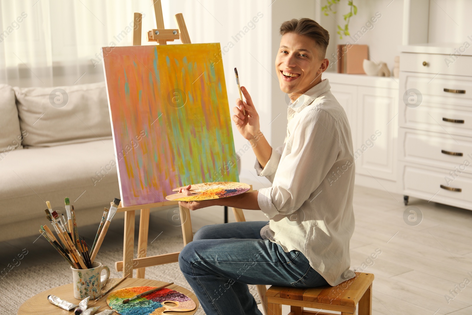 Photo of Smiling man with palette and paintbrush drawing abstract picture at home