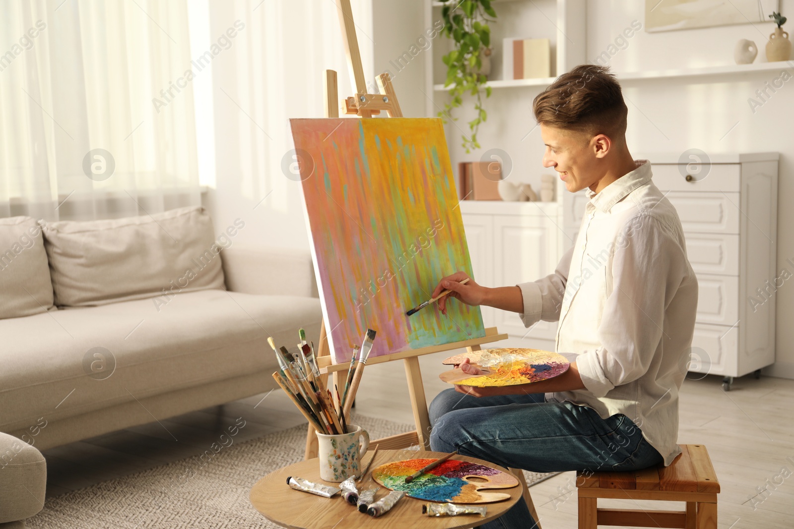 Photo of Smiling man with palette and paintbrush drawing abstract picture at home. Space for text