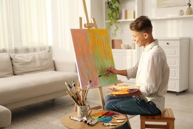 Smiling man with palette and paintbrush drawing abstract picture at home. Space for text