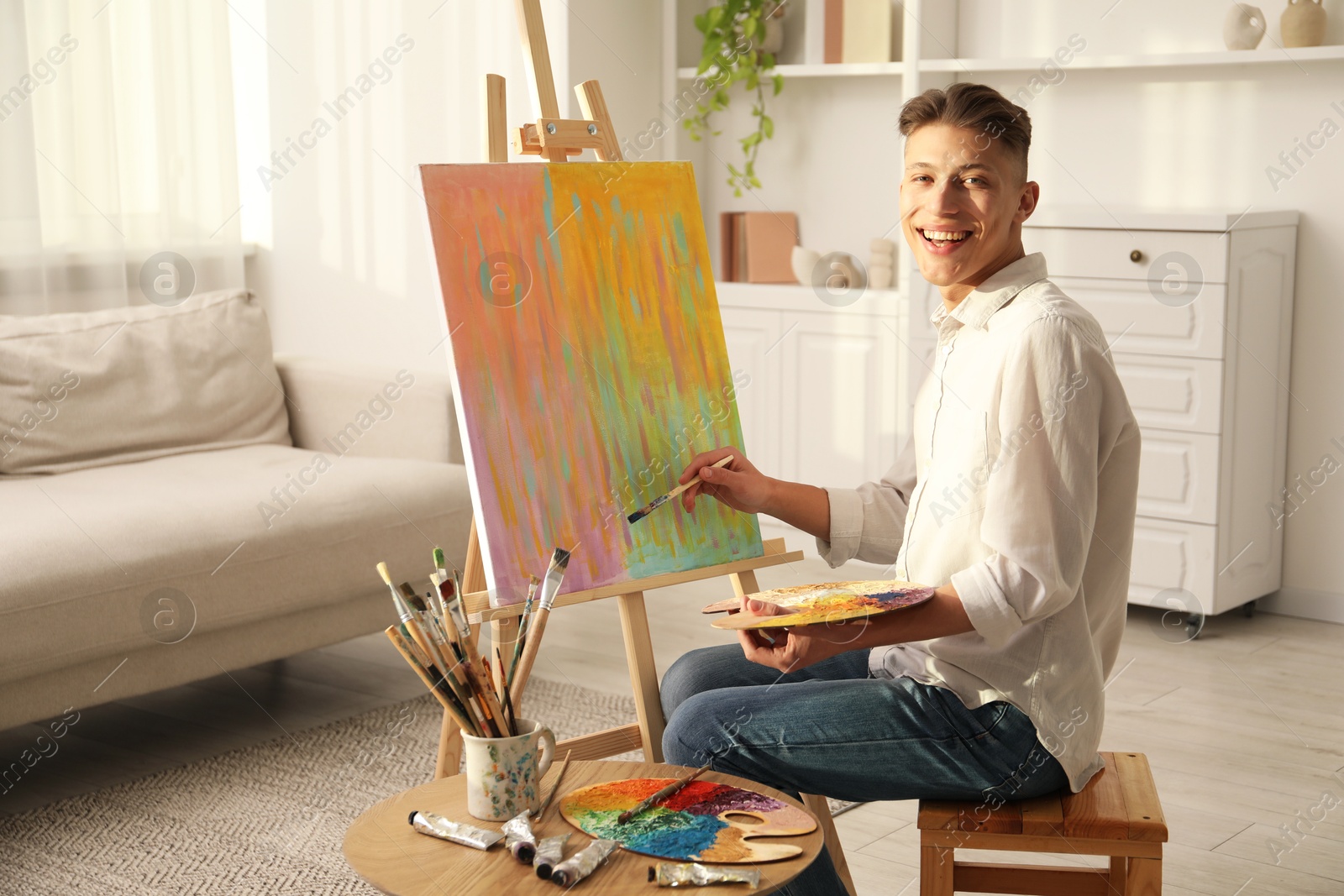 Photo of Smiling man with palette and paintbrush drawing abstract picture at home