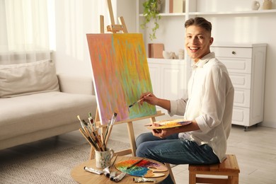 Photo of Smiling man with palette and paintbrush drawing abstract picture at home