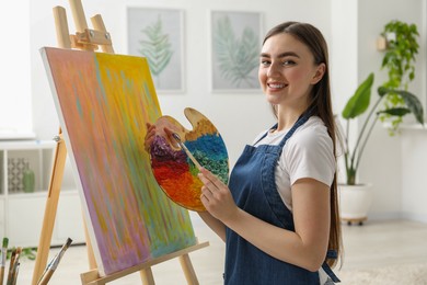 Smiling woman with palette and paintbrush drawing abstract picture