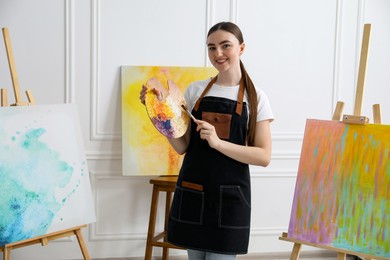 Photo of Smiling woman with palette and paintbrush in workshop