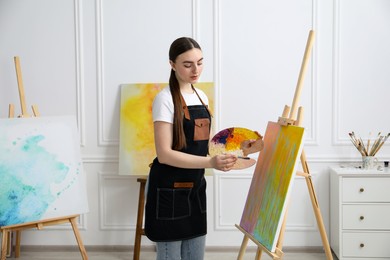 Beautiful woman with palette and paintbrush drawing abstract picture in workshop