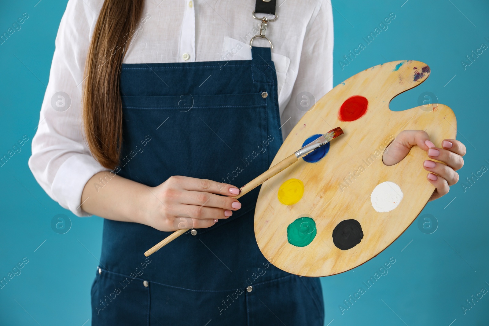 Photo of Woman with wooden palette and paintbrush on light blue background, closeup