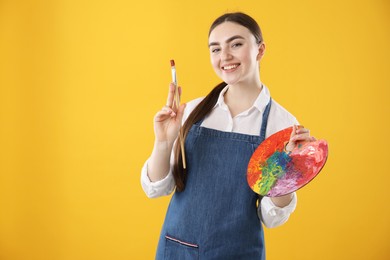 Smiling woman with palette and paintbrush on orange background. Space for text