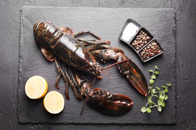 Photo of Raw lobster, cut lemon, microgreens and spices on dark textured table, top view