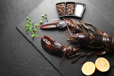 Photo of Raw lobster, cut lemon, microgreens and spices on dark textured table, top view