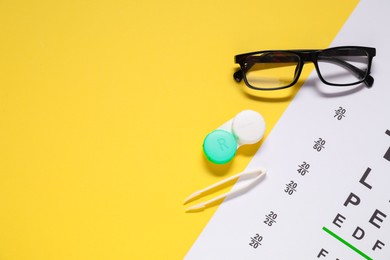 Glasses, vision test chart, lenses and tweezers on yellow background, flat lay. Space for text