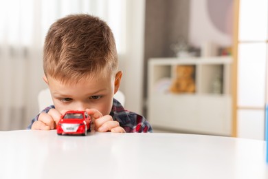 Photo of Little boy playing with toy car at table indoors