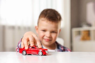 Little boy playing with toy car at table indoors, selective focus