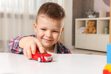 Little boy playing with toy car at table indoors