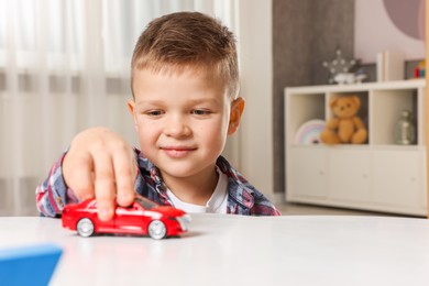 Photo of Little boy playing with toy car at table indoors