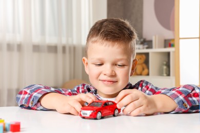 Little boy playing with toy car at table indoors