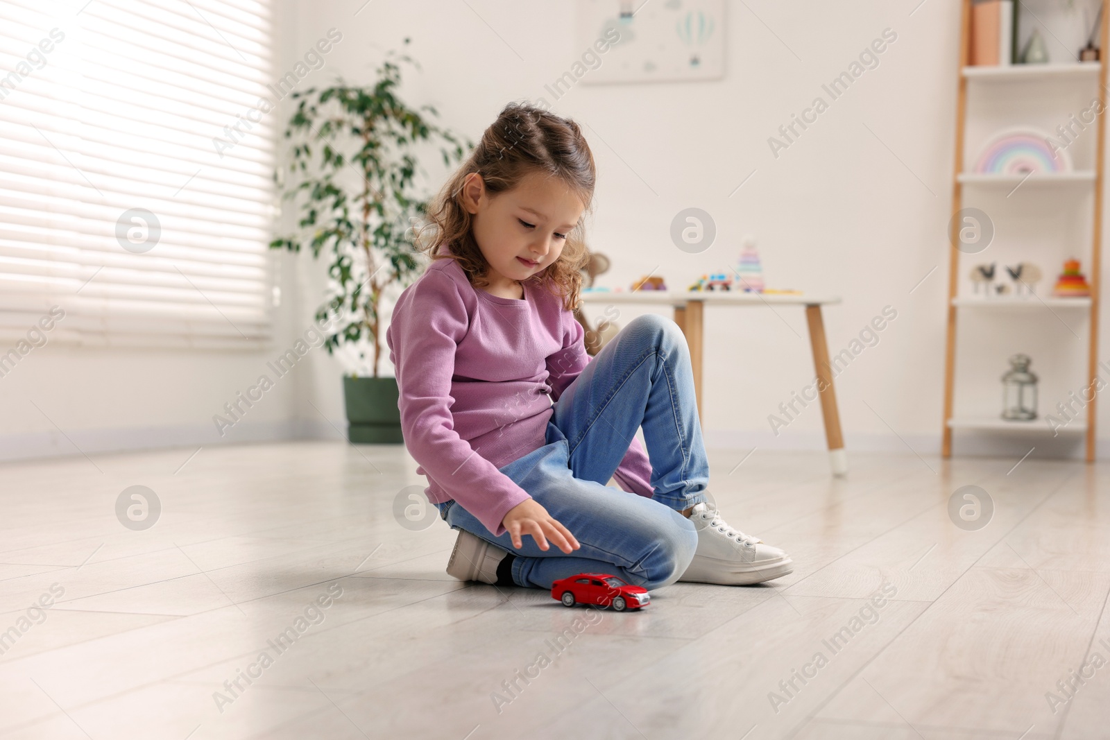 Photo of Little girl playing with toy car on floor at home