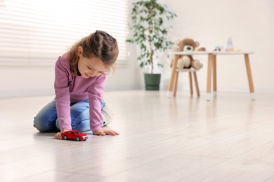 Photo of Little girl playing with toy car on floor at home, space for text