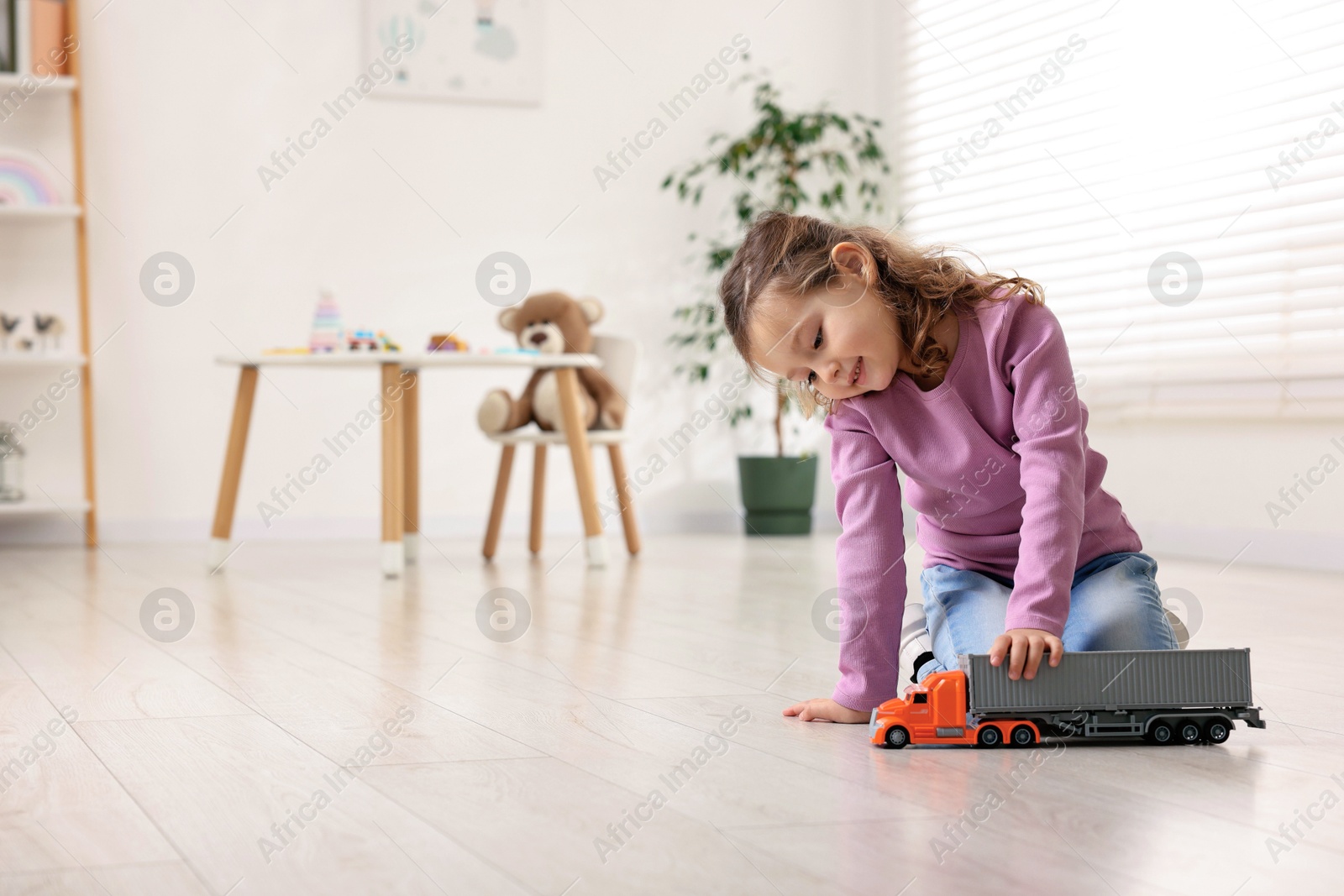 Photo of Little girl playing with toy car on floor at home, space for text