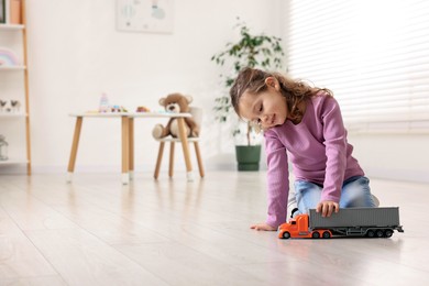 Little girl playing with toy car on floor at home, space for text