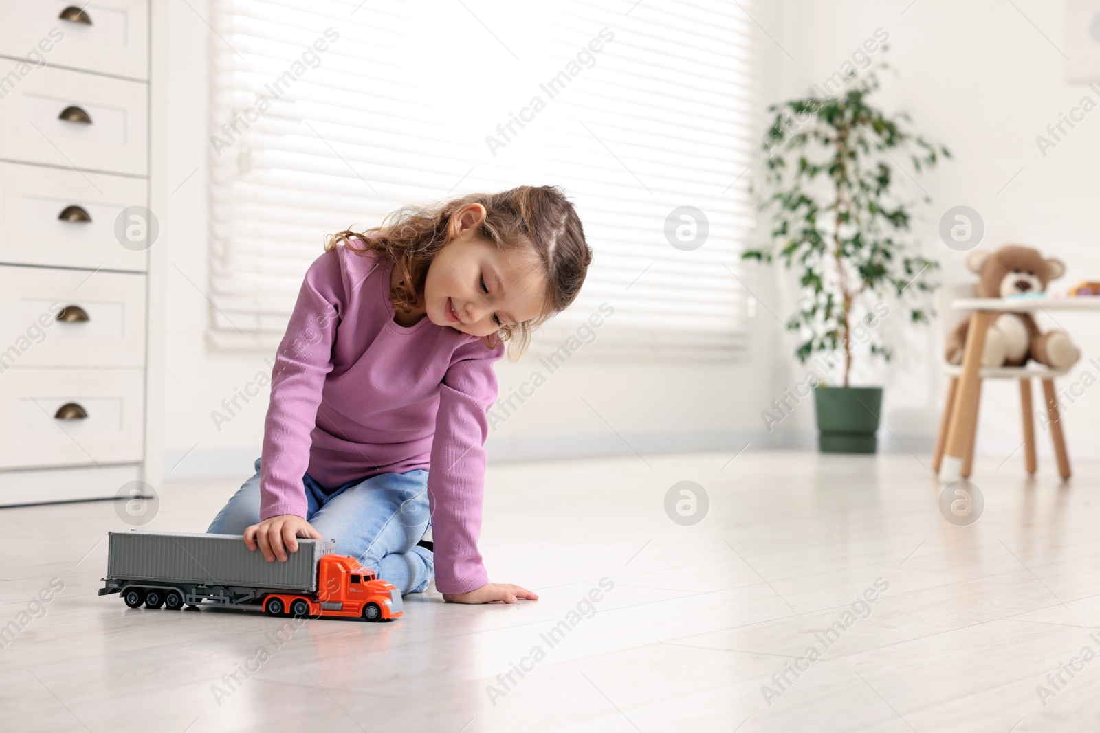 Photo of Little girl playing with toy car on floor at home, space for text