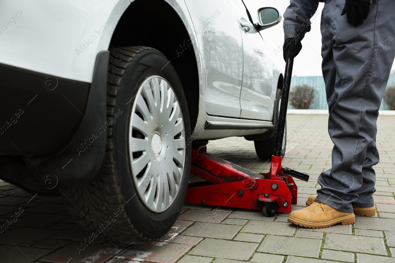 Photo of Auto mechanic lifting car with scissor jack outdoors, closeup