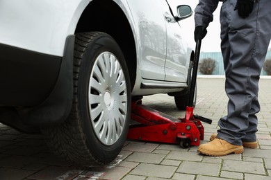 Auto mechanic lifting car with scissor jack outdoors, closeup