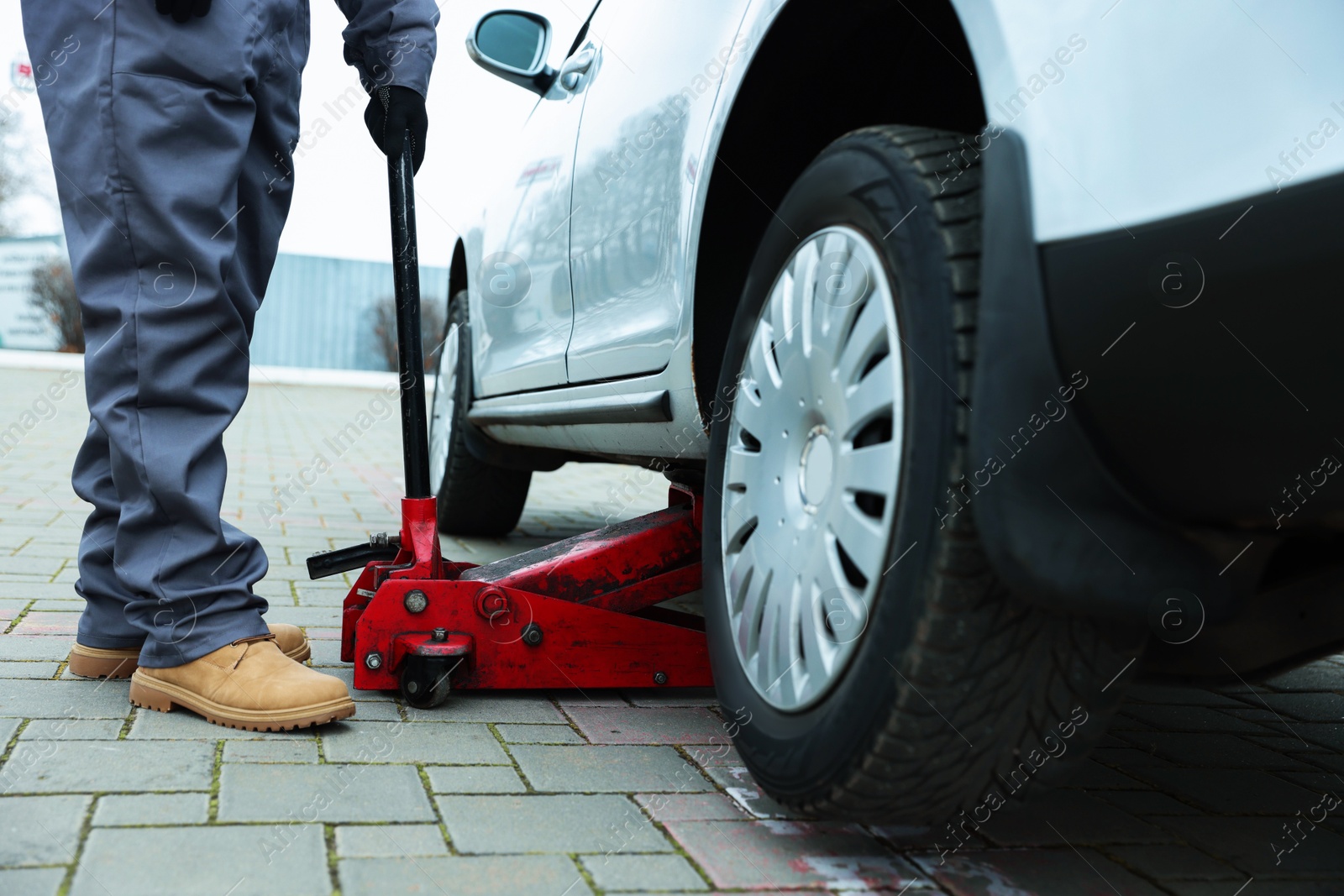 Photo of Auto mechanic lifting car with scissor jack outdoors, closeup