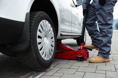 Photo of Auto mechanic lifting car with scissor jack outdoors, closeup